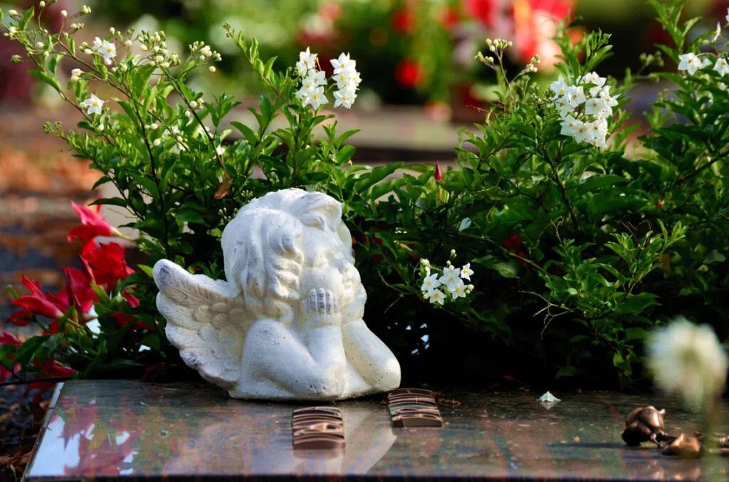 Statue d'ange pensive posée sur une pierre tombale fleurie